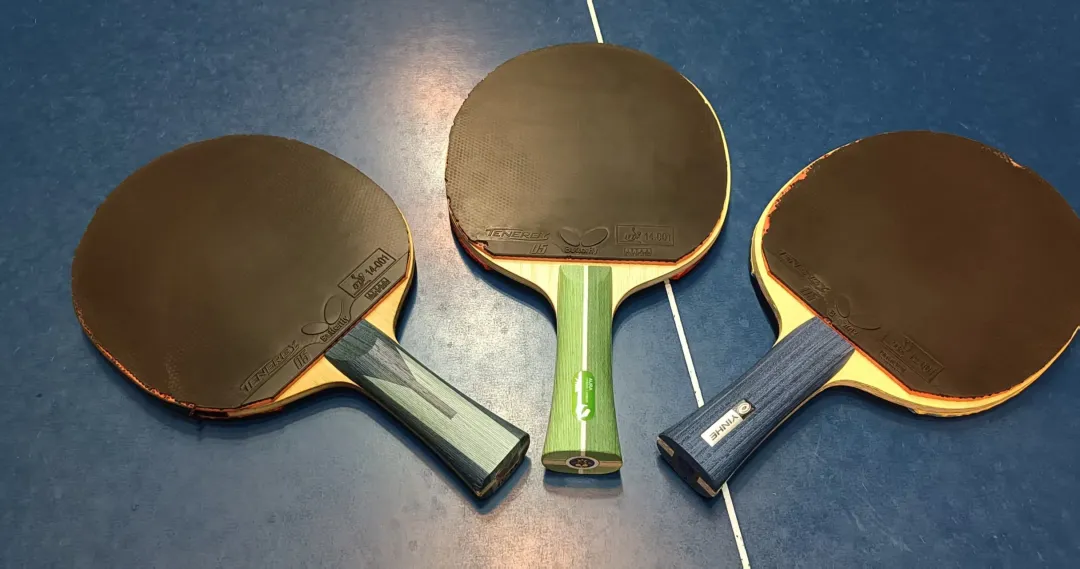 Three table tennis paddles displayed on a blue table with different handle styles